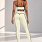 A woman shown from the back wearing a matching pale yellow activewear set with black trim, consisting of a sports bra and high-waisted leggings, standing in a bright studio.