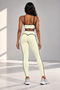 A woman shown from the back wearing a matching pale yellow activewear set with black trim, consisting of a sports bra and high-waisted leggings, standing in a bright studio.